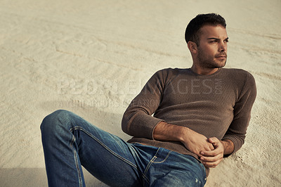 Buy stock photo A handsome male model reclining on the desert sand in trendy clothing