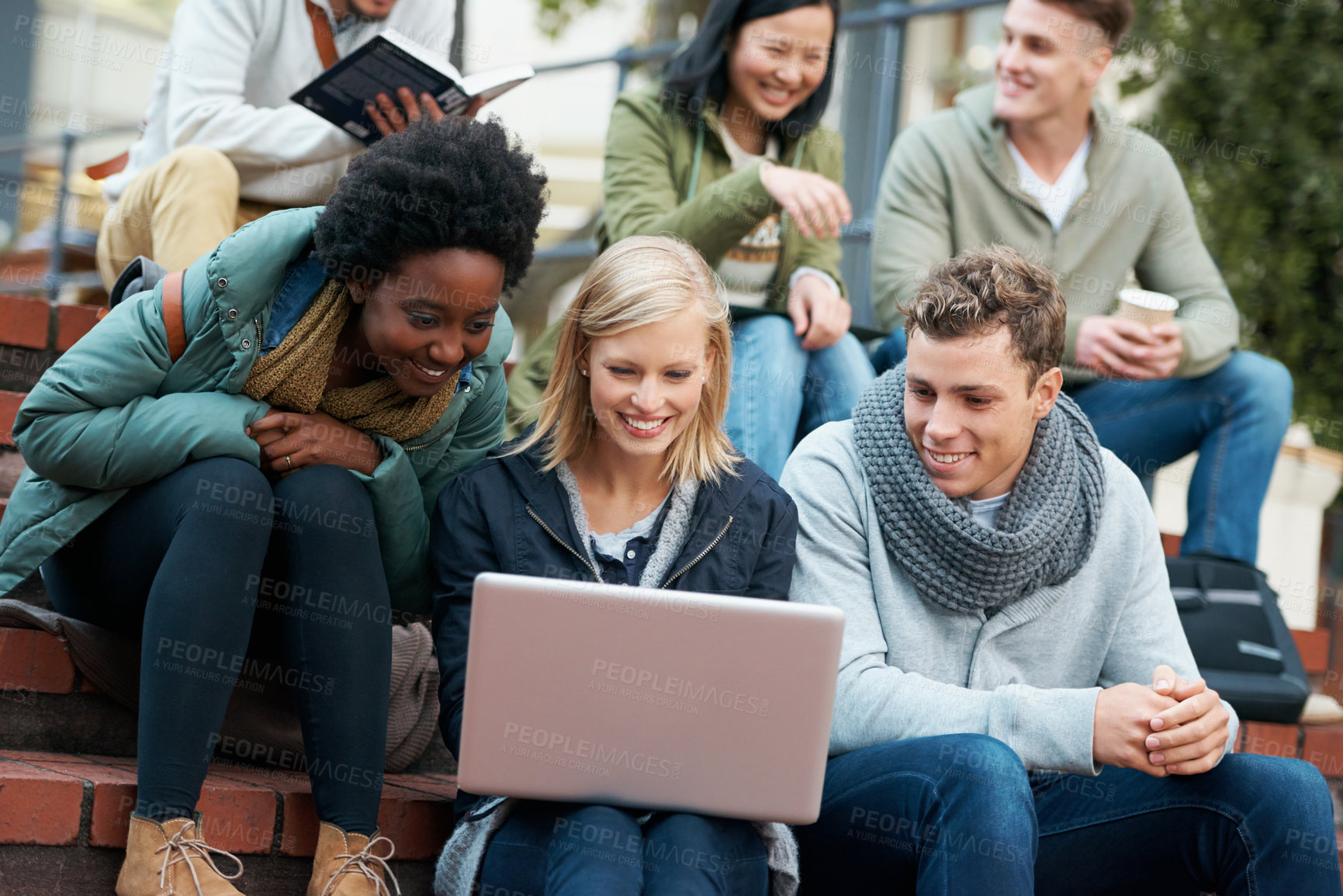 Buy stock photo Shot of a group of smiling university students looking at something on a laptop