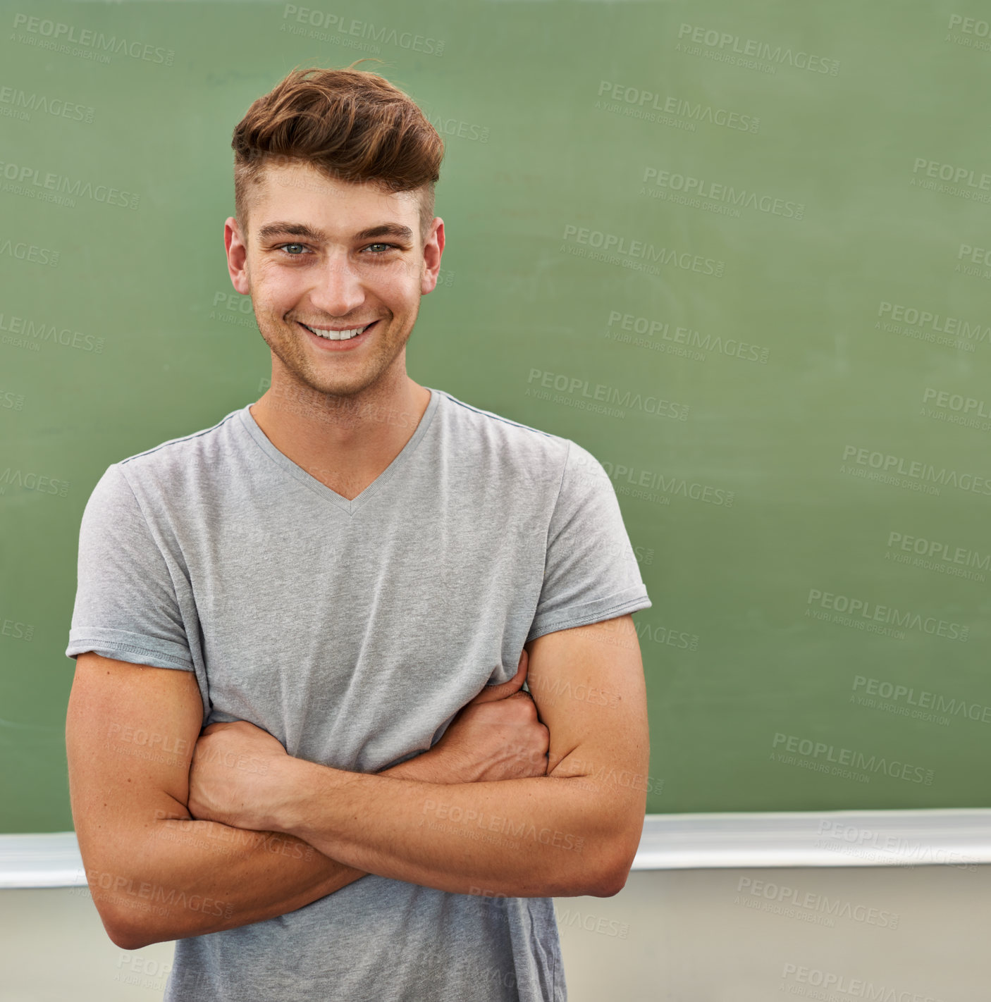 Buy stock photo A young man smiling at the camera while standing in front of a blackboard