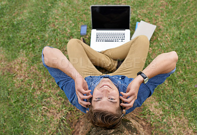 Buy stock photo High angle shot of a young man sitting in front of a laptop outside and listening to music