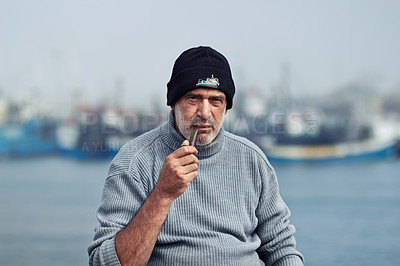 Buy stock photo Fisherman portrait, smoking and man in nature with pipe by the sea water at a port for fishing. Old male, ocean and mature dock worker sitting by boats outdoor with tobacco product at harbor work