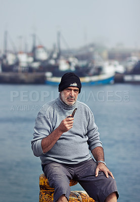 Buy stock photo Fisherman, mature man portrait and smoking pipe by the sea water at a port for fishing. Old man, ocean and senior dock worker sitting by boats outdoor with tobacco smoke at a harbor for work