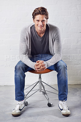 Buy stock photo Man, portrait and smile on chair with fashion on wall background for style, confidence or relax. Male person, face and sitting or casual in jeans in studio for happiness in Canada, clothes or outfit