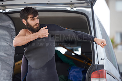 Buy stock photo A young man putting on his wetsuit before a surf