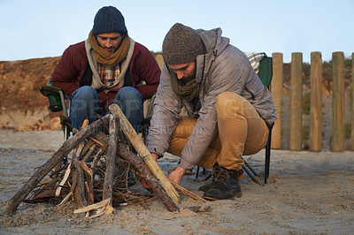 Buy stock photo Two young men building a fire on the beach