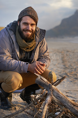 Buy stock photo A young man building a fire on the beach