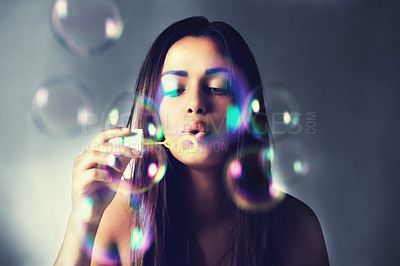 Buy stock photo Shot of a beautiful young woman blowing bubbles in the studio