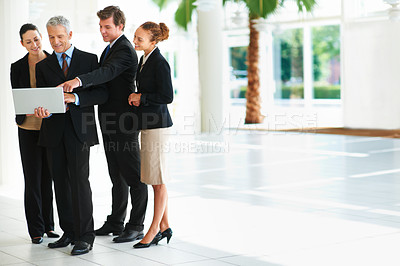 Buy stock photo Shot of a group of businesspeople talking over a laptop while standing in an office lobby