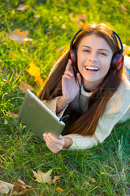 Buy stock photo An attractive young woman listening to music on her digital tablet while outdoors