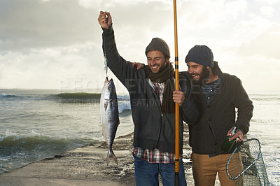 Buy stock photo Shot of two young men fishing at the beach