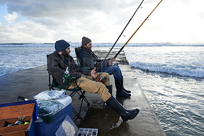 Buy stock photo Shot of two young men fishing off a pier