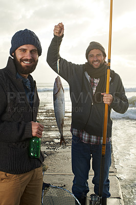 Buy stock photo Shot of two young men fishing off a pier with a fish on a line