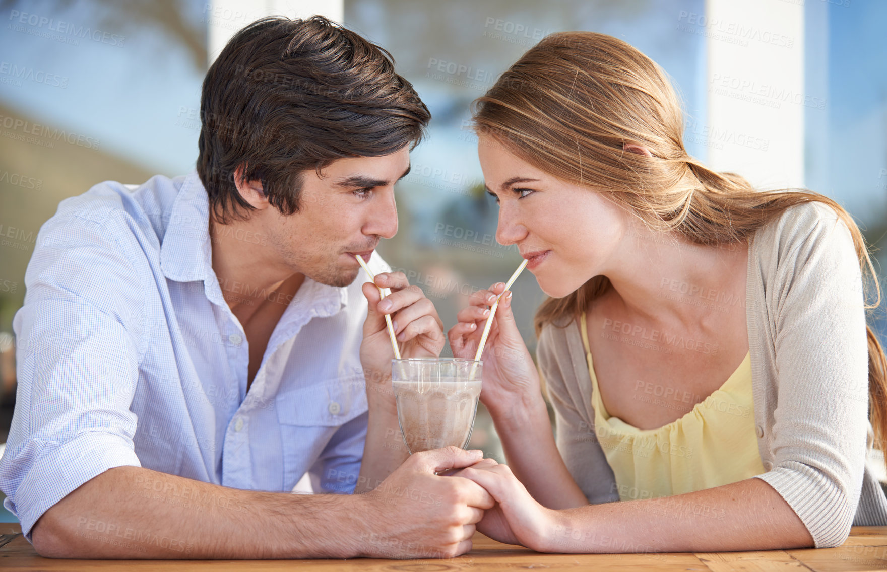 Buy stock photo A young couple sharing a chocolate milkshake while on a date