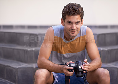 Buy stock photo A young man sitting outside looking at you while holding a camera