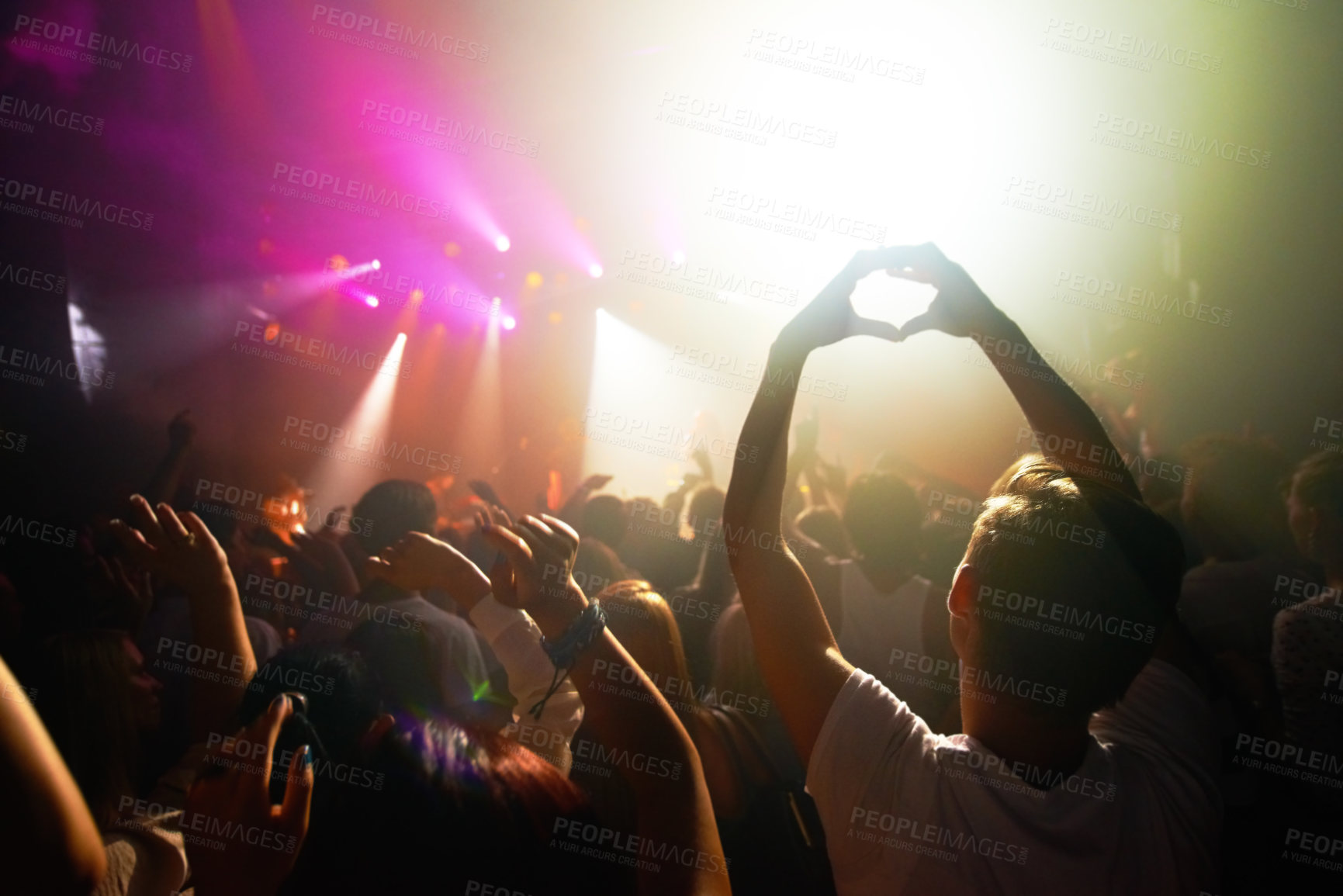 Buy stock photo Crowd at concert, music and watch band performance, music festival, light and energy with audience back view. People dance with hands in heart shape, musician on stage and festival in Florida.