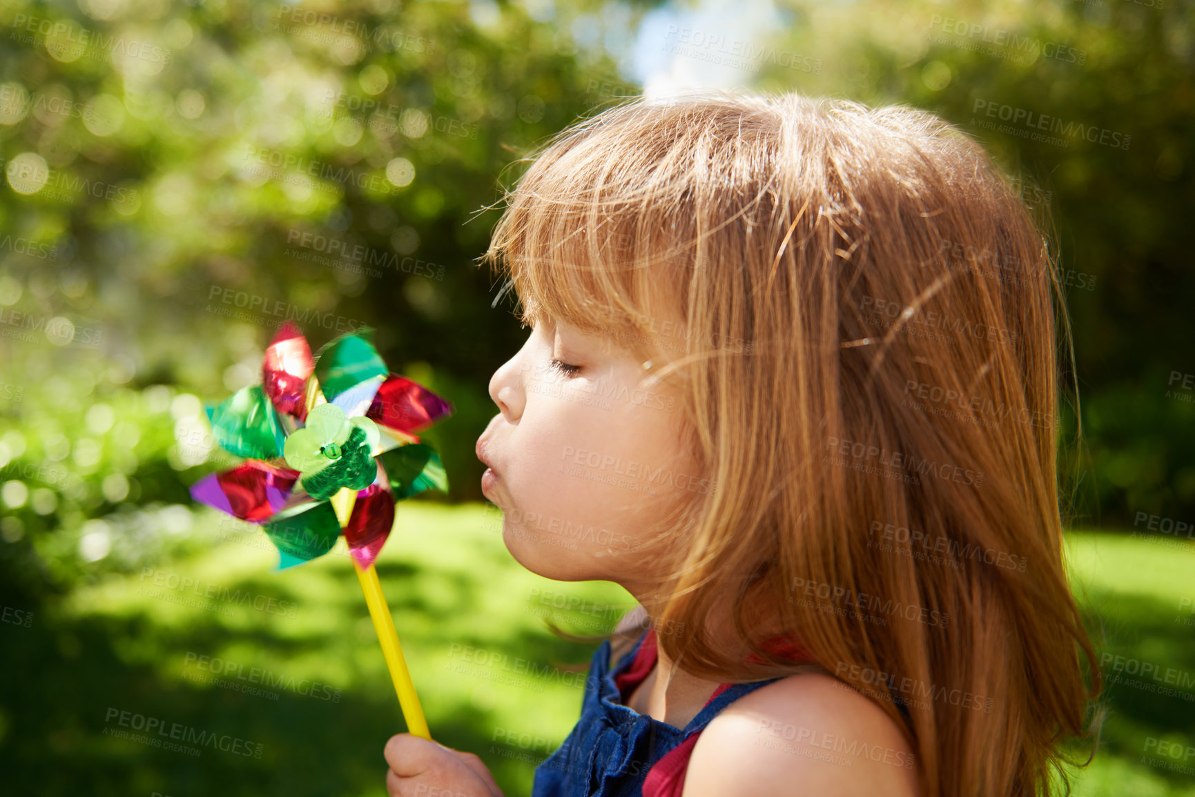 Buy stock photo Young girl, outdoor and blowing pinwheel, garden and enjoying freedom of outside and happy. Pretty little child, backyard and summer for playing, toy and windmill for school holidays and happiness