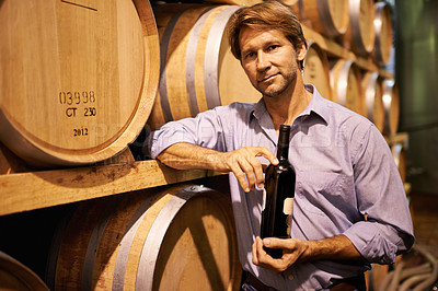 Buy stock photo Portrait of a handsome mature man standing in a wine cellar with a bottle of wine