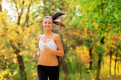 Buy stock photo Shot of a positive-looking young woman jogging in a park in autumn