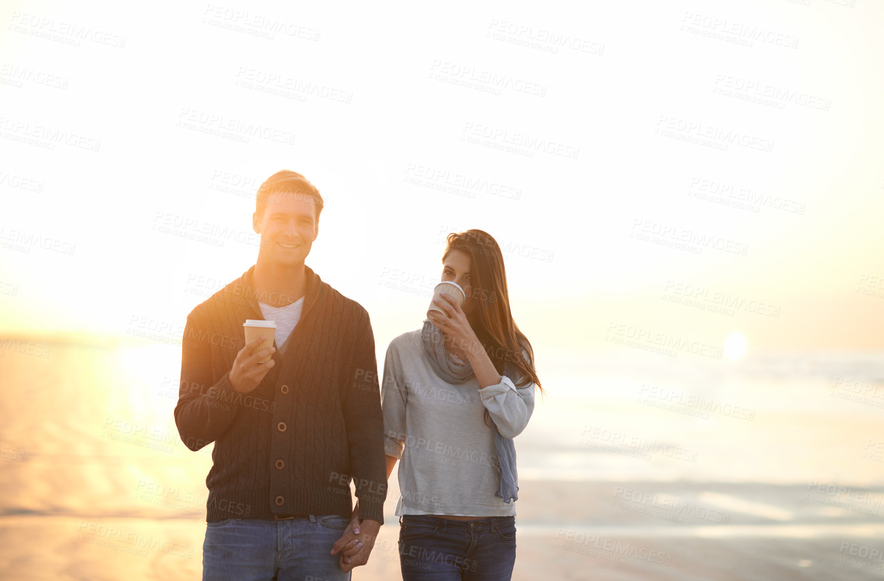 Buy stock photo Couple, coffee and walk at beach on vacation, sunset and holding hands in portrait by ocean. Man, woman and drink with tea cup with smile, bonding and happy for memory on holiday by sea in Australia