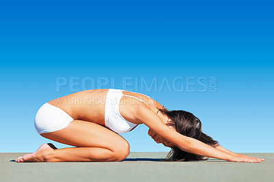 Buy stock photo A fit young woman doing yoga while against a blue sky