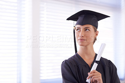 Buy stock photo Shot of a young woman in a graduation gown holding a diploma and looking off to the side