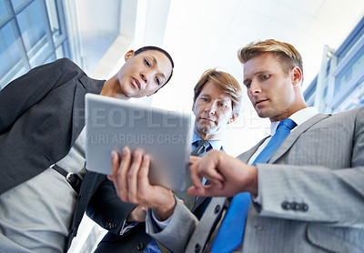 Buy stock photo Low-angle view of a young businessman showing his colleagues something on a tablet