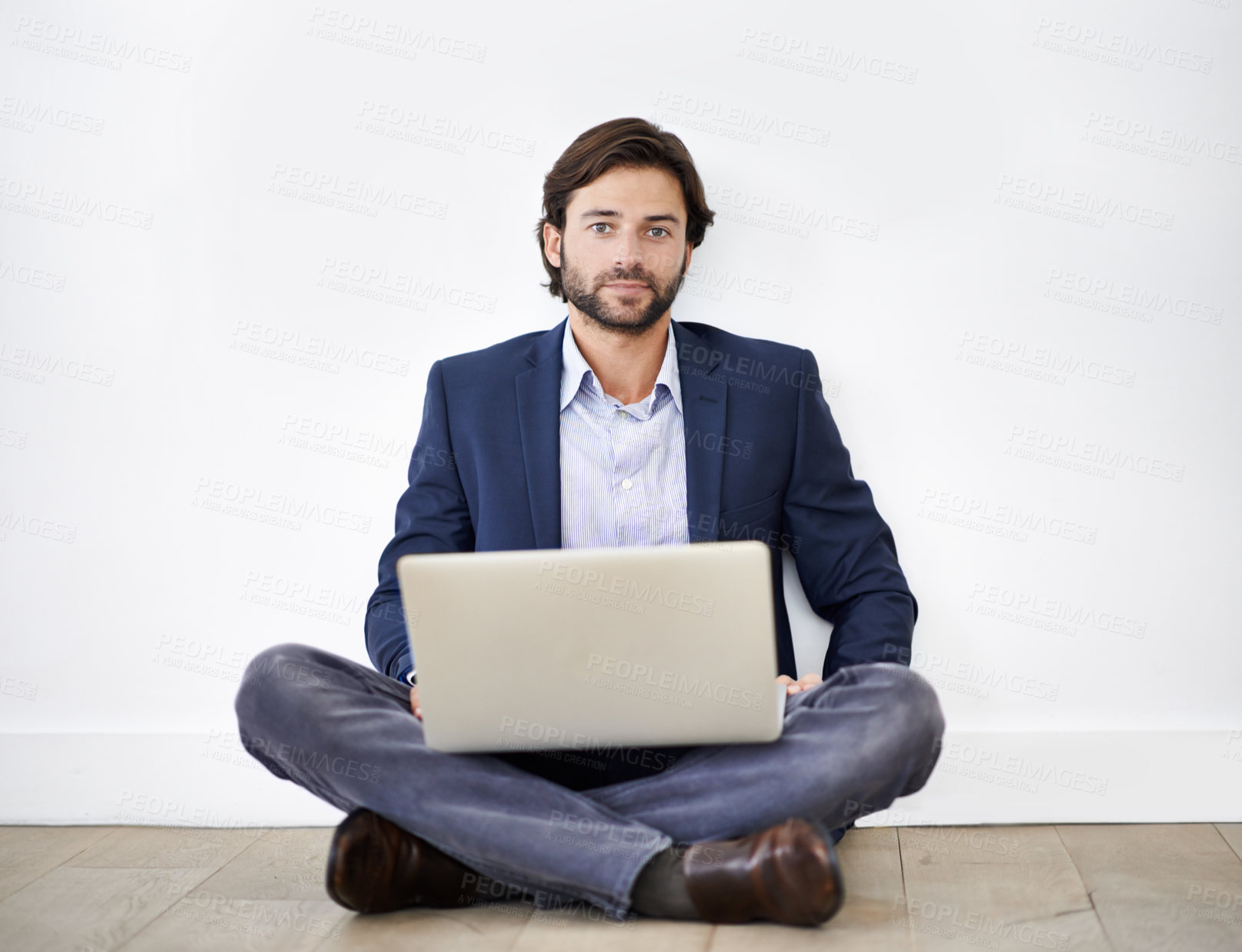 Buy stock photo Portrait shot of a handsome young businessman sitting cross-legged on the floor with his laptop