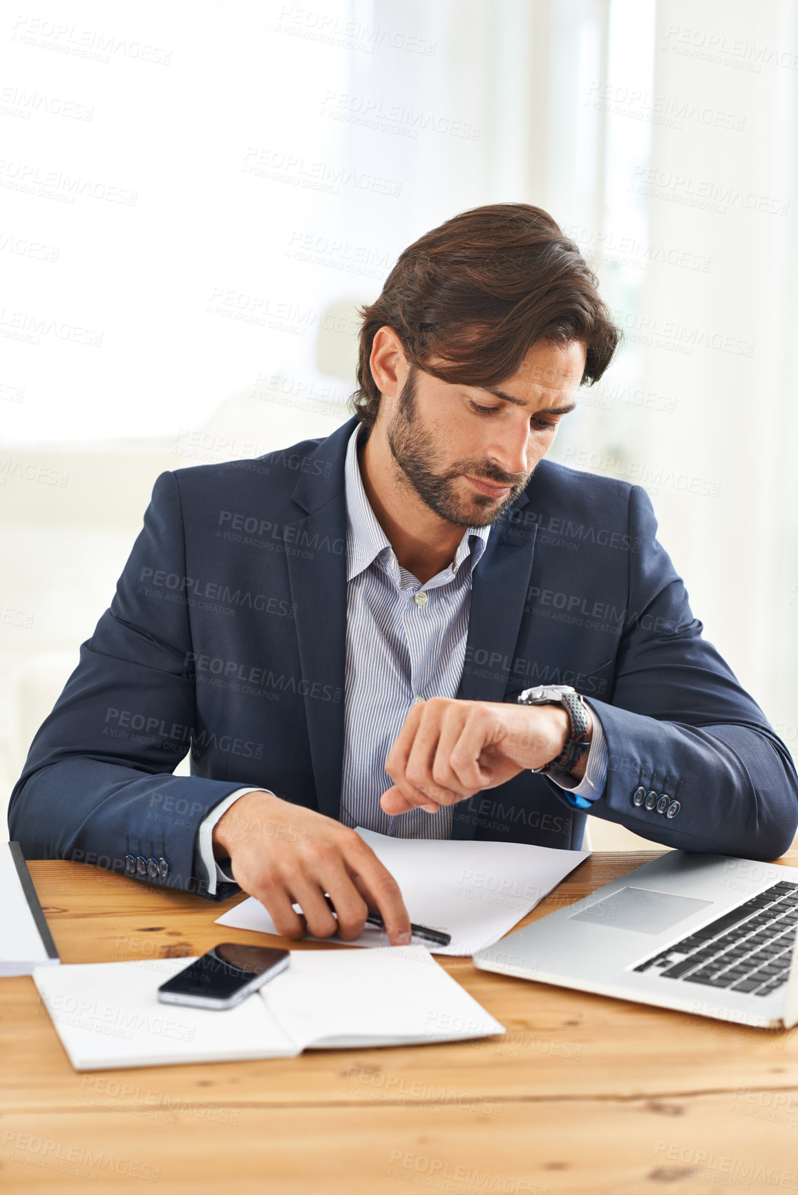 Buy stock photo A handsome businessman looking at his watch while working on his laptop