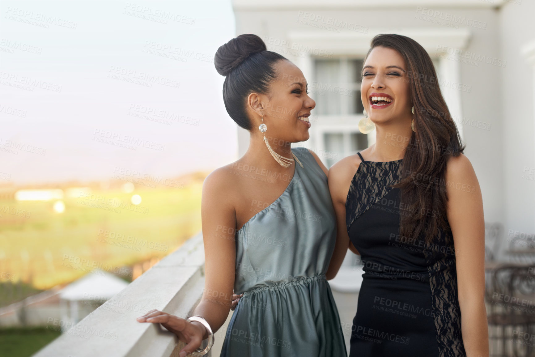 Buy stock photo Two young women in evening wear standing on a balcony