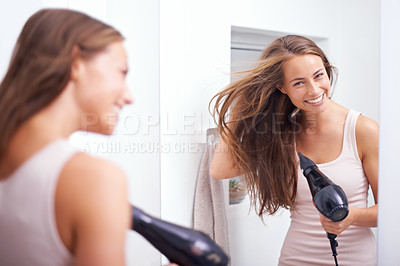 Buy stock photo A young woman blow drying her hair in front of a mirror