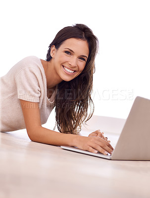Buy stock photo A young woman smiling at the camera as she lies on the floor with a laptop
