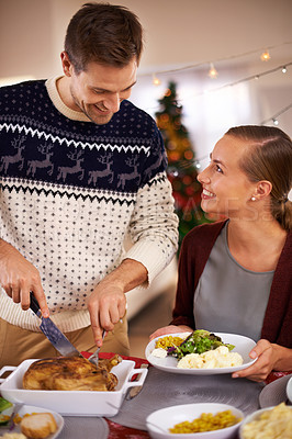 Buy stock photo Christmas, happy couple and eating dinner in home, smile or bonding together at party. Xmas, man or woman at table for food at festive celebration, relax or people on holiday cutting chicken for meal