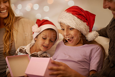 Buy stock photo A little girl unwrapping a Christmas present while surrounded by her family