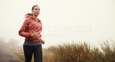 Buy stock photo A young woman running along a road on a misty morning