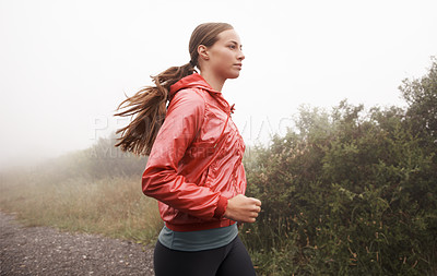 Buy stock photo Shot of a young female jogger in a misty country road in the morning