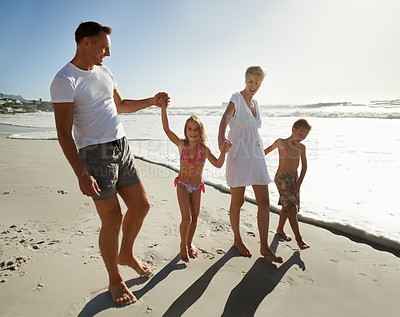 Buy stock photo A happy young family walking down the beach together in the sunshine