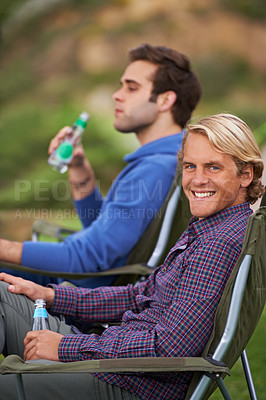Buy stock photo Camping, man and portrait with drinks for relax on grass in nature with happiness for holiday and vacation. People, smile and alcohol at campsite in woods for adventure, travel and bonding in forest