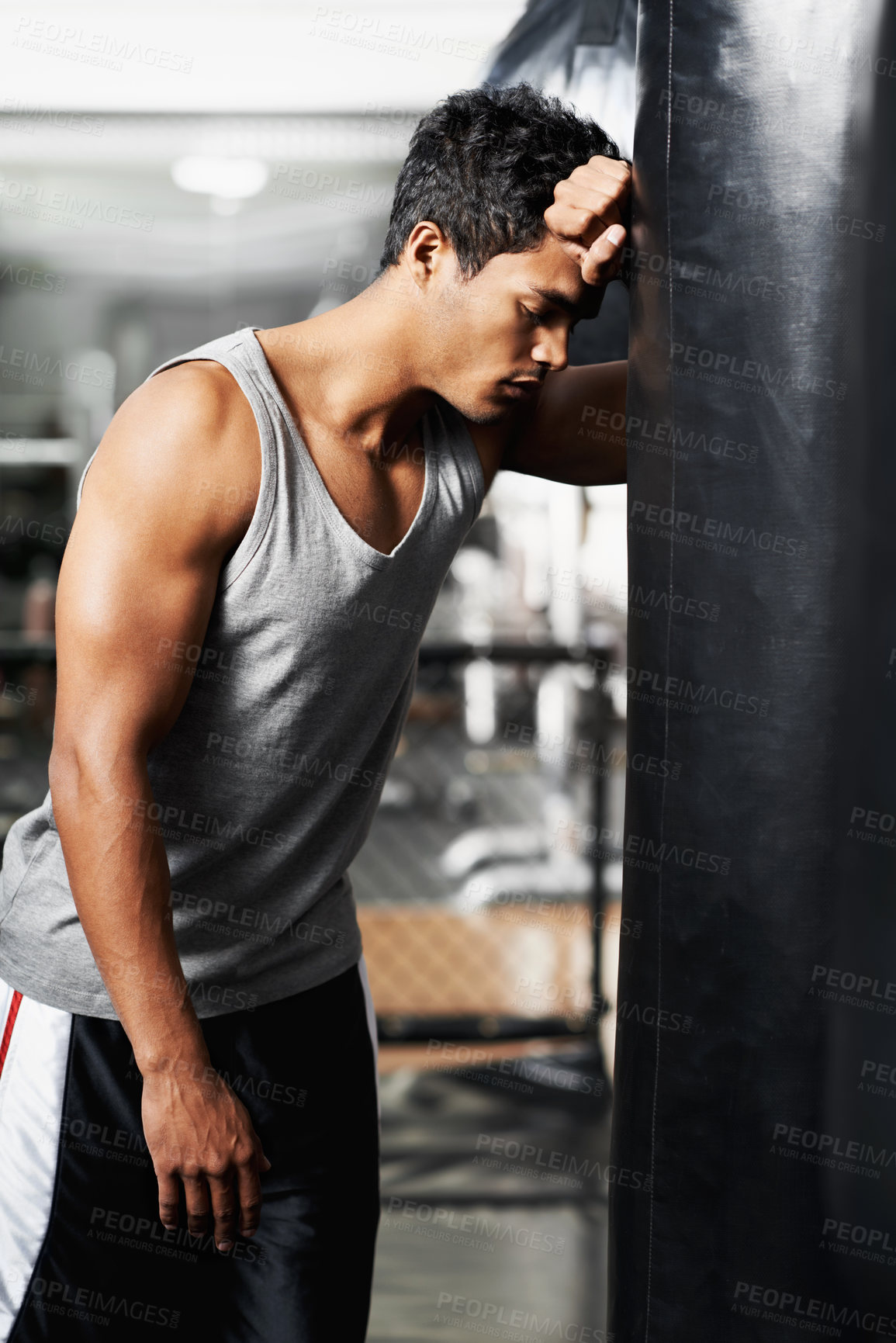 Buy stock photo A muscular young man leaning against a boxing bag and looking defeated