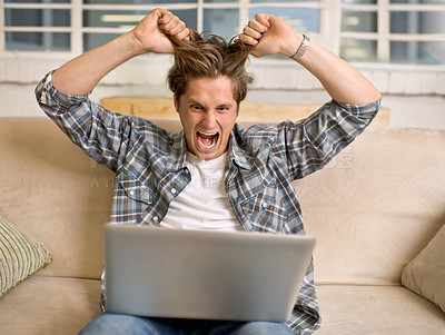 Buy stock photo A young man looking frustrated while working on his laptop