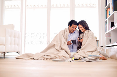 Buy stock photo Shot of a young couple sitting on the floor wrapped in a blanket looking at photo albums
