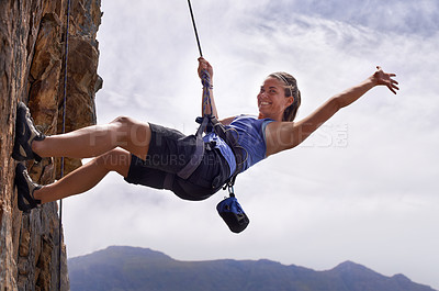 Buy stock photo Shot of a young woman hanging by a rope while rock climbing