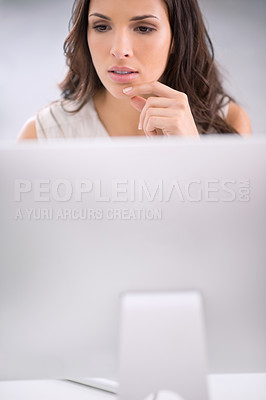 Buy stock photo Young, serious and thinking businesswoman on a computer working on solving a business problem. Professional caucasian corporate female sitting and doing research for a company project on a modern pc