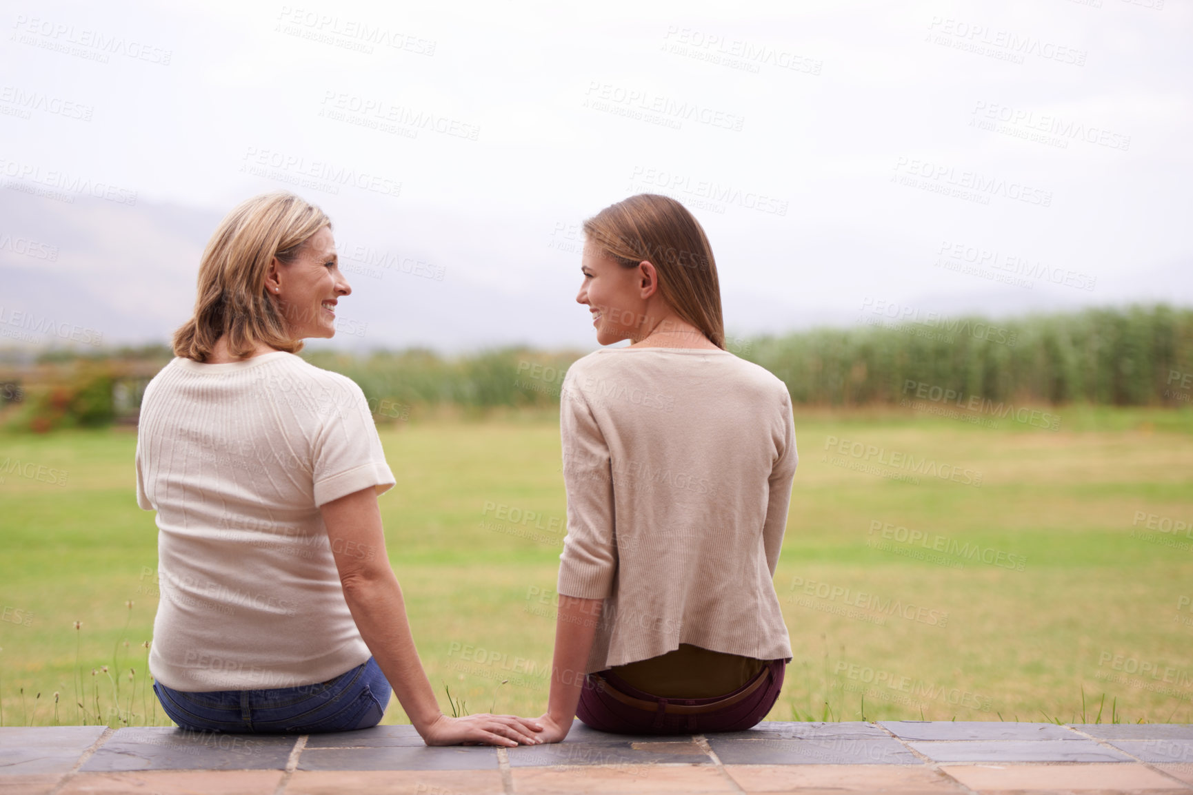 Buy stock photo Women, mother and daughter with garden, back and conversation in morning with bonding, love and care. People, girl and family for talking, chat or relax together on patio by grass lawn in countryside