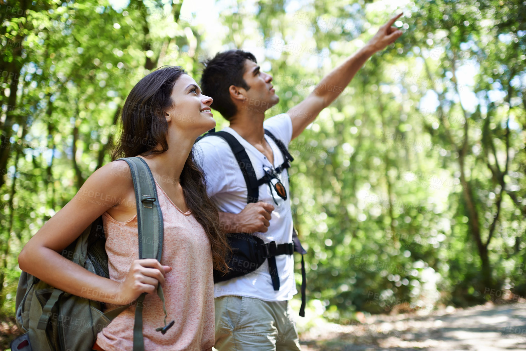Buy stock photo Happy couple, backpack and pointing with direction for sightseeing, destination or hiking together in nature. Young man and woman with smile, bag and showing path or route for trekking in forest