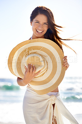 Buy stock photo A beautiful young woman wearing a sarong and holding a woven sunhat at the beach