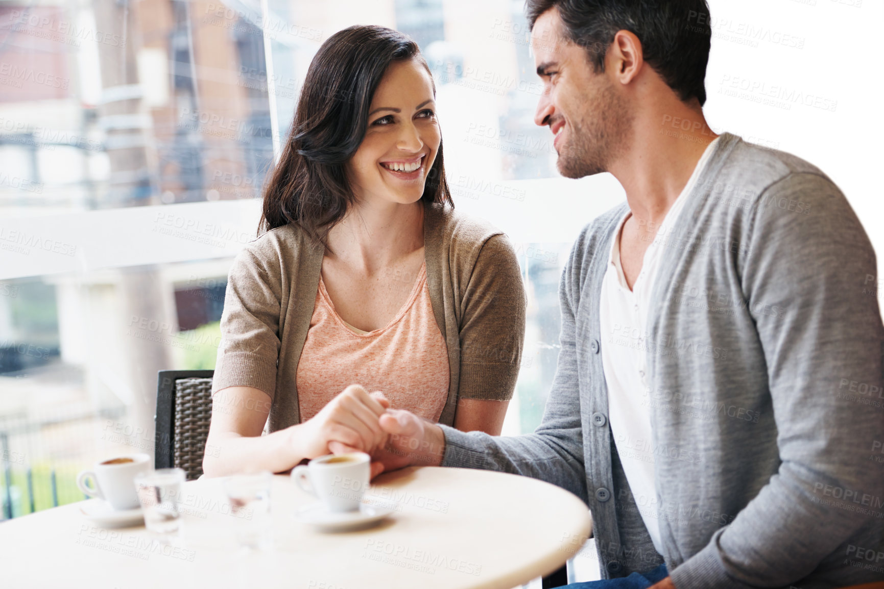 Buy stock photo Happy couple, holding hands and love in coffee shop on holiday and bonding together on espresso date. Man, woman and care in restaurant with cappuccino, water and romantic in bistro with commitment