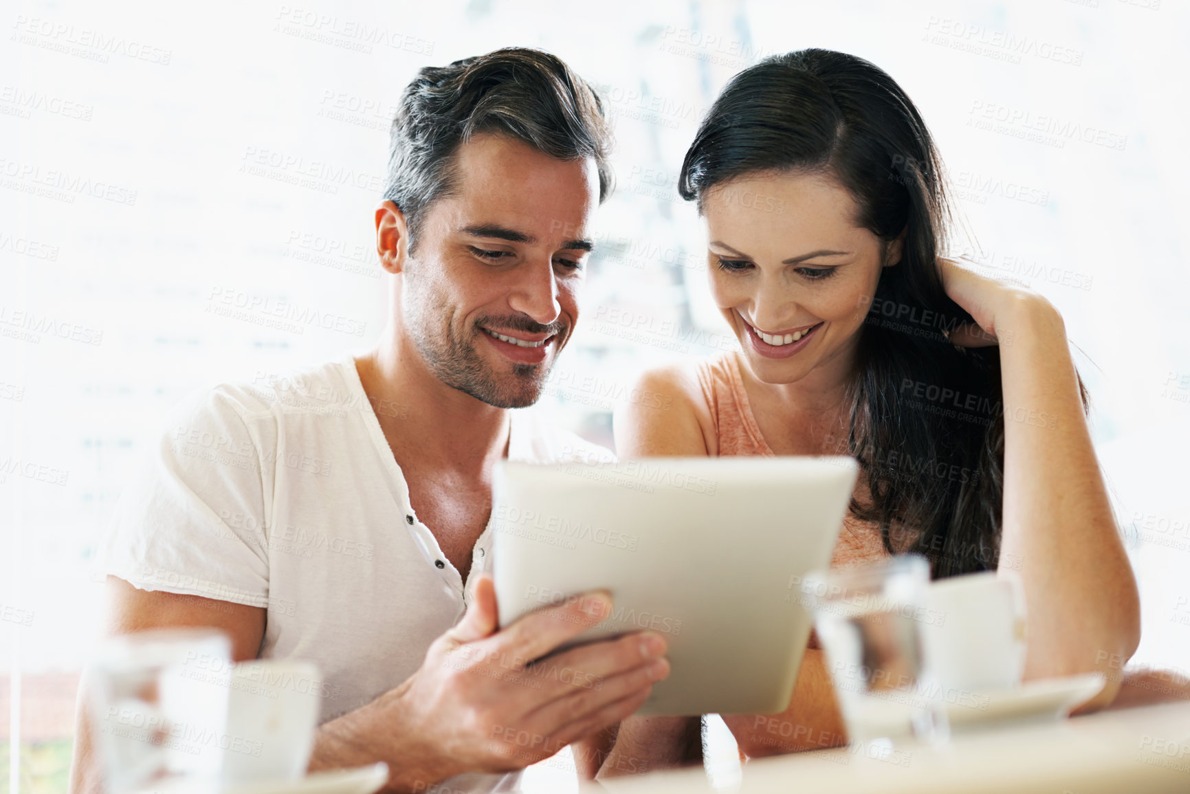 Buy stock photo Shot of a young couple using their tablet during a coffee date
