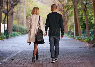Buy stock photo Full length rearview shot of a young couple walking hand in hand in a park
