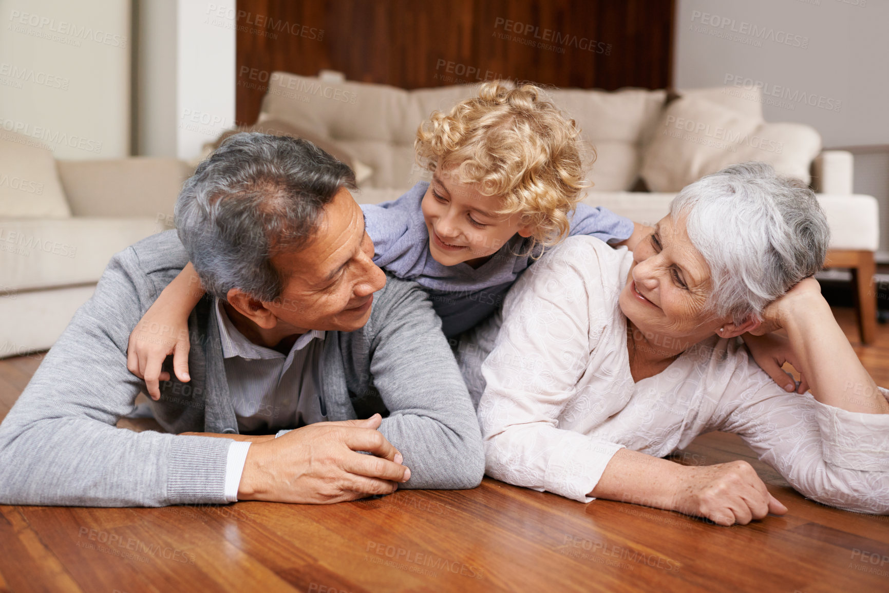 Buy stock photo A little boy lying on top of his grandparents on the floor of their living room