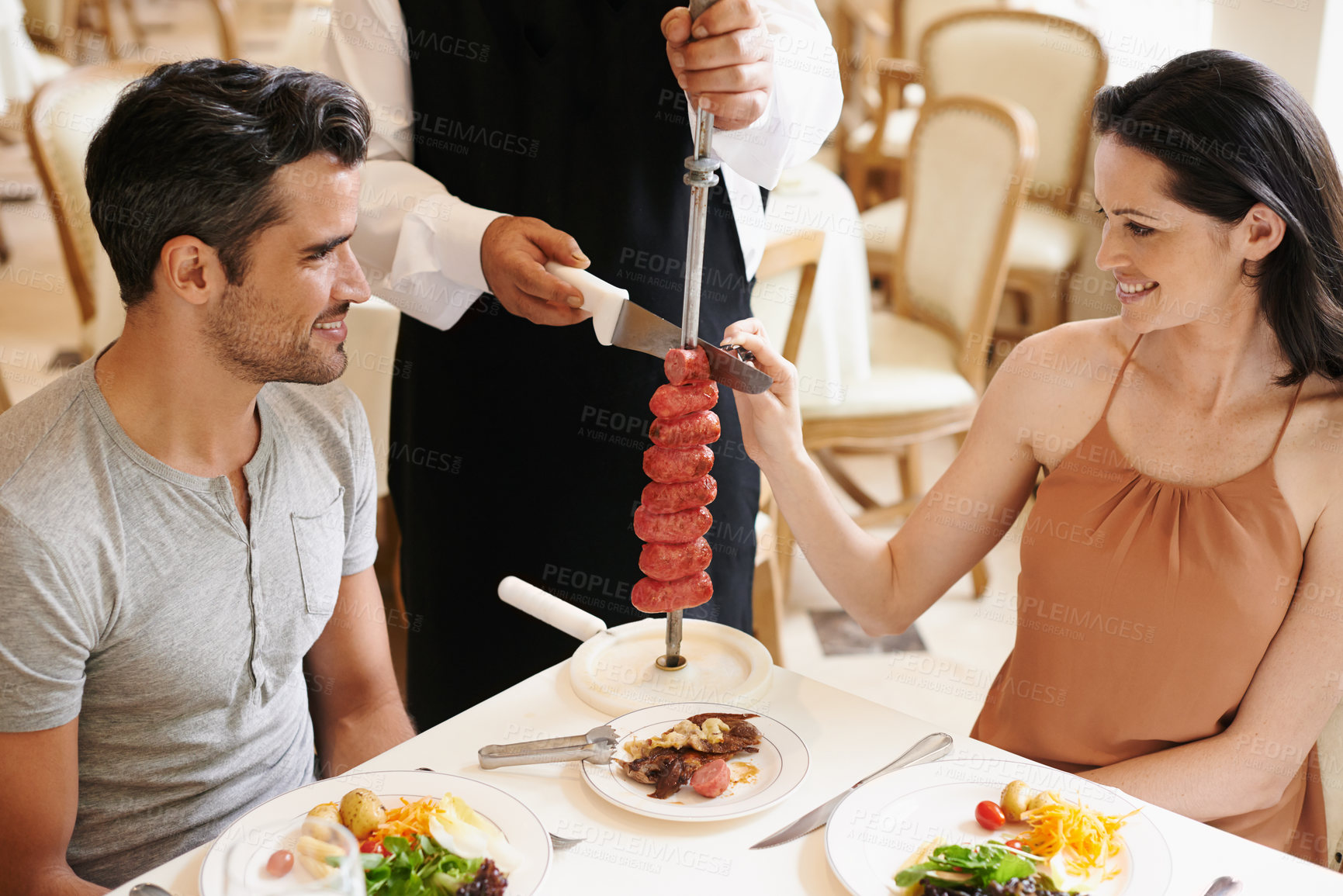 Buy stock photo Couple, restaurant and waiter serving food or sausage kebab on skewer for fine dining, anniversary or nutrition. Man, woman and relationship bonding dates in Italy with water carving, meal or eating